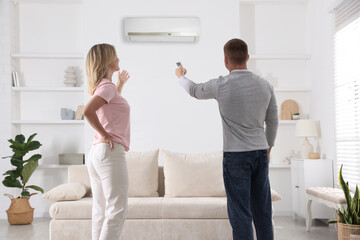 Fototapeta premium Couple at home. Man switching on air conditioner with remote control