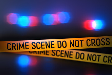 Closeup view of yellow crime scene tape with police car lights flashing in the background at night. Focus on the tape with bokeh, blur and lens glow creating dramatic investigation mood