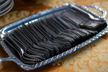 Neatly arranged black disposable plastic forks on a silver serving tray