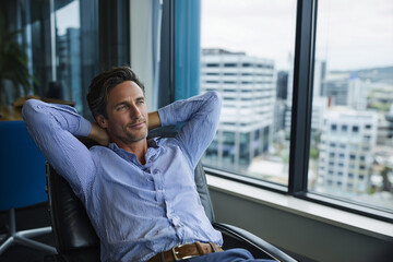  Contemplation of Success: A composed professional gazes thoughtfully through an office window, arms relaxed, visualizing future achievements.