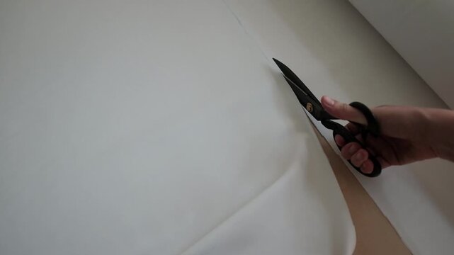 Close up of female hands carefully cuts cotton fabric with scissors. Minimal sewing environment, highlighting manual sewing manufacture. Working process in a small business sewing workshop.