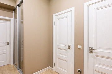 Interior of a hallway with white doors and beige walls, featuring a sliding closet
