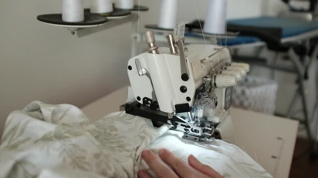 Woman sews bed linen or clothes on overlock sewing machine. Manufacture of textile goods. Professional sewing skills. Factory for production of clothing and textile goods.