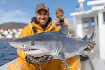 Smiling fisherman holding a small shark on a fishing boat. A successful catch during a sea angling adventure. Close-up of marine wildlife.