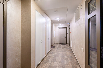 Bright hallway with beige textured walls, white cabinets, and tile flooring. A door is at the end of the hall with a window at the other end