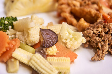 Close-up of various cooked vegetables including baby corn, broccoli, carrots, mushrooms, and cauliflower on a plate.