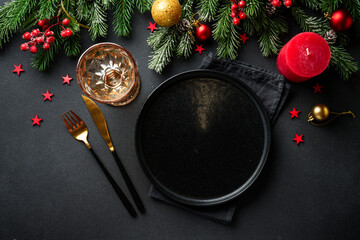 Christmas table setting. Christmas dinner - black plates with cutlery and decorations on black background.