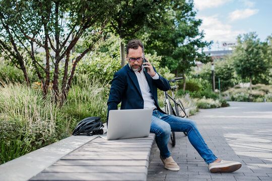 Manager working in urban park, making phone call and typing on laptop.