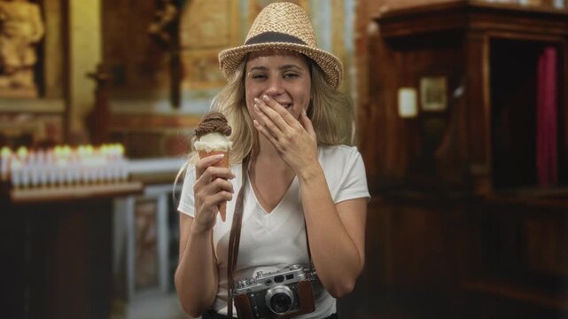 Woman wearing straw hat and camera around neck holding ice cream cone, hand to mouth in church building; travel joy.
