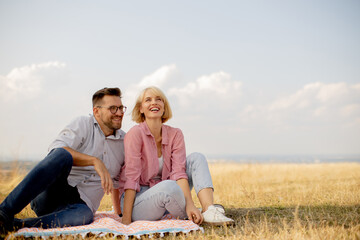 Couple enjoys a sunny day outdoors while sitting on a blanket in a field, sharing laughter and smiles together