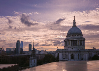 Naklejka premium St Paul's Cathedral dome and cross standing prominent in the London skyline. Reflecting the glow of a dramatic sunset with modern buildings and construction cranes shaping the evolving urban landscape