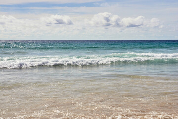 Tranquil ocean waves meeting sandy shore under clear sky on peaceful beach day with gentle clouds.