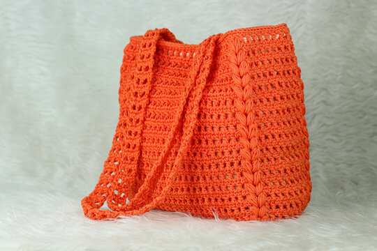 Crocheted handmade orange bag on furry white blanket.