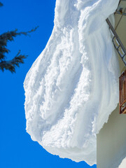 A close-up view of a massive snow cornice on a roof against a clear blue sky (Shiga Kogen, Nagano, Japan)