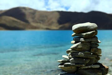 Stacked Rocks by Blue Lake with Mountains, Turquoise Water Under Cloudy Sky