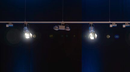 Professional studio spotlights hanging from the ceiling illuminate a dark stage background in a modern production setup.