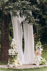 A Beautiful Outdoor Wedding Setup with Elegant White Drapery, Stunning Floral Arrangements, and a Stylish Golden Accent Table Surrounded by Lush Greenery in a Serene Landscape