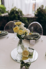Elegant Table Setting with Floral Arrangement and Lemon Accents for a Refined Dining Experience in a Bright, Natural Setting with Greenery as Backdrop and Soft Lighting