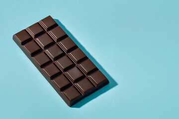 This dark chocolate bar rests on a blue backdrop, showcasing glossy squares and a premium, indulgent look.