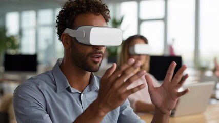 A man wearing a virtual reality headset is looking at a computer monitor. A woman is sitting behind him - Powered by Adobe