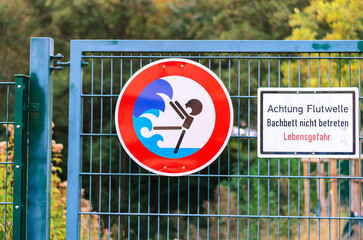 Warning signs on a metal fence for flash flood danger in a stream bed