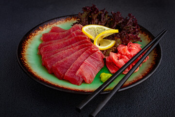 Fresh tuna sashimi served with lemon, wasabi, and pickled ginger on a dark background