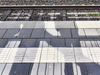 Long shadows of people waiting for a train on a railway platform