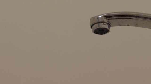 Close-up of water drop dripping from faucet in bathroom, plumbing system malfunction at home, water leakage from dripping tap