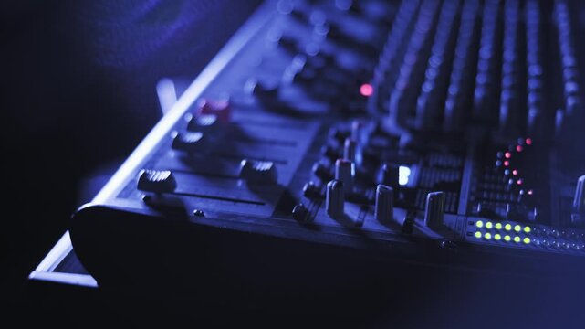 Low angle shot of professional audio mixer console, showing illuminated knobs and faders with active LED meters, set in a dark environment with moody blue lighting and subtle lens flare effects.