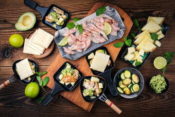 Traditional authentic swiss raclette with chicken filet meat, pineapple, avocado and savoy cheese served as top view on a wooden design board