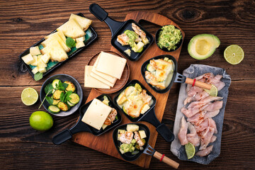 Traditional authentic swiss raclette with chicken filet meat, pineapple, avocado and savoy cheese served as close-up on a wooden table