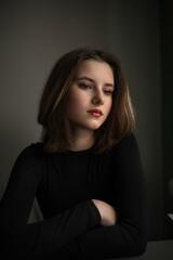 Fototapeta premium Young woman with shoulder-length hair, wearing a black top, gazes thoughtfully with soft lighting, capturing a moment of introspection and beauty in a serene atmosphere