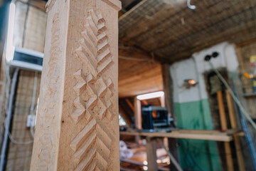Close-up of a wooden pillar with traditional geometric carvings inside a rustic workshop or house...