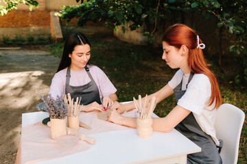 Two women enjoy a pottery class outdoors, shaping clay with smiles and creativity. 2 Girls sculpt clay in an outdoor workshop. Clay art workshop outdoors.