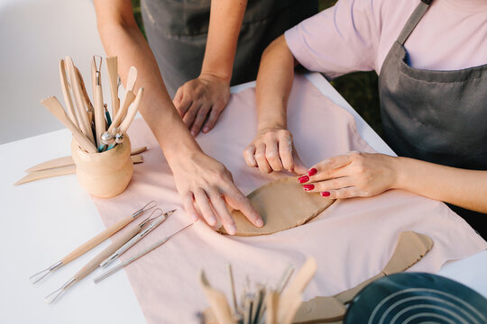 Pottery Workshop Teaching. Pottery instructor guides student in clay shaping during an outdoor ceramic workshop. Ceramic training highlights clay art practice, with teacher guiding pottery students.