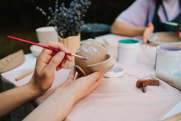 Artist paints delicate purple fish on a handmade clay mug. Painting ceramic mug with purple fish using brush and paint. Ceramic painting of mug with fish pattern using brush strokes.