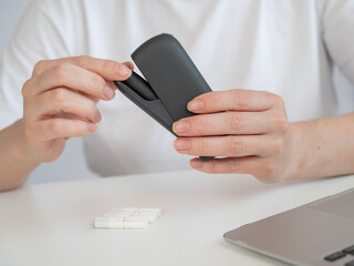 A woman smokes an electronic cigarette while working on a laptop. Tobacco heating system.