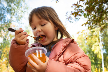 Close-up of a child holding a dessert and eating it with a fork in the park. Quick snack.