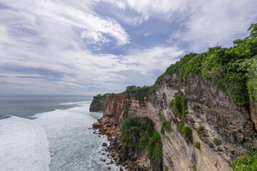 Rocky cliff overlooking the ocean with a few small waves in the distance