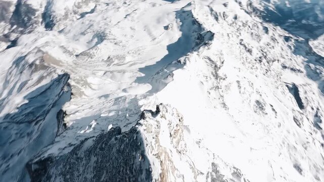 FPV drone diving down a steep, snowy mountain ridge.