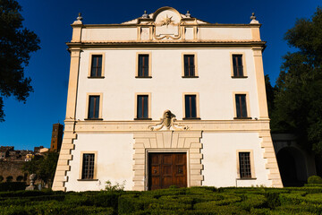 Elegant historic villa with symmetrical facade, wooden door and formal garden under a clear blue sky