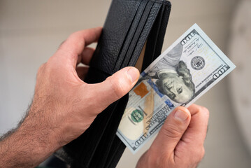 Hand pulling one US 100 bill from wallet. Concept of expense, payment, banking, or budget management. Ideal for financial or consumer themes.