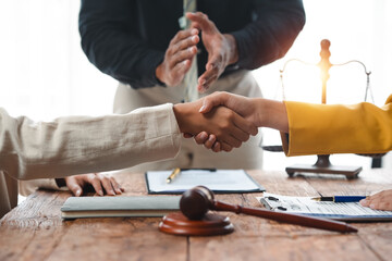 Two parties making a legal agreement, shaking hands in partnership with lawyer present. Gavel and scales of justice on desk