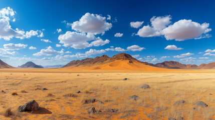 Naklejka premium Scenic desert landscape under a blue sky with scattered clouds. Arid mountains and dry grasslands create a serene panorama.