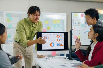 Asian business professionals discussing marketing data and financial charts on a computer screen during a corporate office meeting