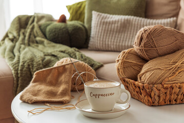 Cozy Living Room with Yarn, Pumpkins, Pillows and Cup of Cappuccino on White Table