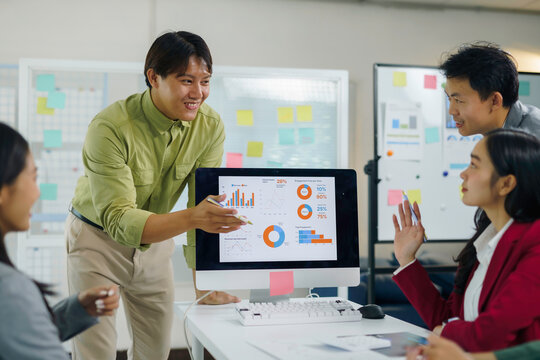 Asian business professionals discussing marketing data and financial charts on a computer screen during a corporate office meeting