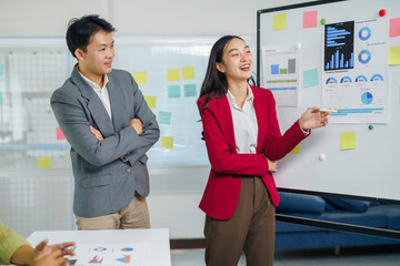 Asian business professionals collaborating in a modern office, a woman presenting data analysis on a whiteboard during a team meeting