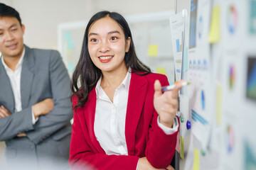 Confident businesswoman presenting data charts and graphs on a board, leading a team meeting in a modern office setup