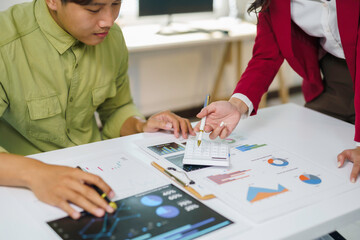 Business partners collaborating in an office, discussing financial charts and graphs on paper and a tablet, using a calculator for analysis